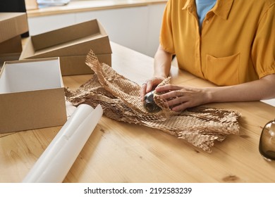Close-up of woman wrapping bottle in paper and packing it in cardboard box at table for delivery