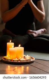 Close-up. Woman In Yoga Lotus Pose Meditating In A Dark Room With Candle Light. Atmosphere Of Relax And Zen. Exercise To Reach Clarity Of Mind And Perfect Body. Wooden Floor, Soft Morning Light