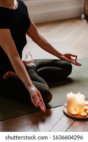 Close-up. Woman In Yoga Lotus Pose Meditating In A Dark Room With Candle Light. Atmosphere Of Relax And Zen. Exercise To Reach Clarity Of Mind And Perfect Body. Wooden Floor, Soft Morning Light