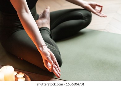 Close-up. Woman In Yoga Lotus Pose Meditating In A Dark Room With Candle Light. Atmosphere Of Relax And Zen. Exercise To Reach Clarity Of Mind And Perfect Body. Wooden Floor, Soft Morning Light
