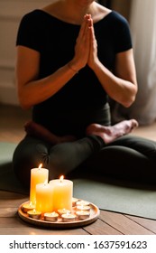 Close-up. Woman In Yoga Lotus Pose Meditating In A Dark Room With Candle Light. Atmosphere Of Relax And Zen. Exercise To Reach Clarity Of Mind And Perfect Body. Wooden Floor, Soft Morning Light