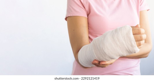 Close-up of a woman's broken arm in a cast. The girl holds a bent arm against the background of a pink t-shirt. Banner, copy space. Insurance medicine concept.