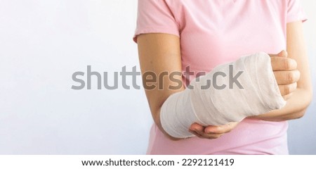 Close-up of a woman's broken arm in a cast. The girl holds a bent arm against the background of a pink t-shirt. Banner, copy space. Insurance medicine concept.
