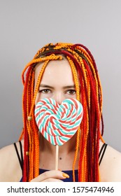 Closeup Of Woman's With Colorful Hair Holding A Heart Lolipop In Front Of Her Face