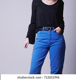 Closeup Of Woman's Fall Winter Fashion Outfit On A Model With Blue Vintage High-waisted Mom Jeans And Black Blouse With Black Belt Isolated On Grey Background. Copy Space.