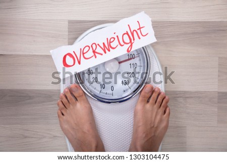 Close-up Of Woman's Feet On Weighing Scale Indicating Overweight On White Paper
