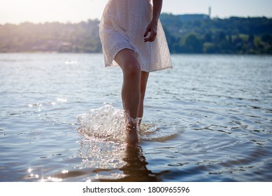  Closeup of woman's feet walking on the beach during a colorful sunset. Woman walking into the river, body part, perfect women's legs, enjoying time on the beach, summer vacation concept