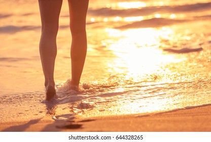 Closeup Of Woman's Feet Walking On The Beach During A Golden Sunset. 