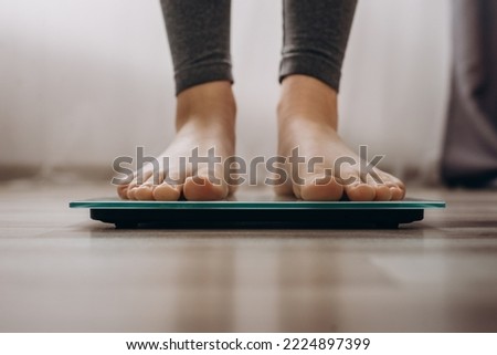 Close-up of woman's feet weighing on scales in living room at home. Female dieting checking and weight loss. Barefoot measuring body fat overweight. Control, wellness, lifestyle and diet concept