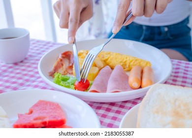 Close-up Of Woman's Hand Eating Breakfast With Sausage, Ham, Bacon, Omelet, Tomato, Toast, And Salad.