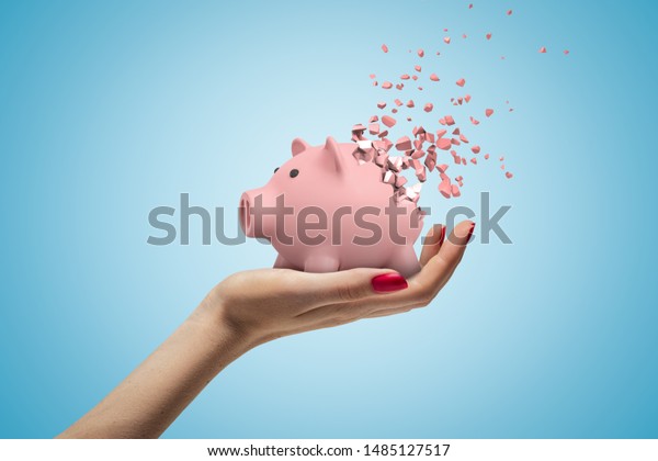 Close-up of woman's hand facing up and holding cute pink piggy bank that has started to disintegrate into pieces on light-blue background. Money worries. Financial difficulties. Profit loss.