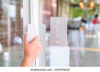 Closeup Woman's Hand Going To Pull The Swing Door To Enter The Cafe, Open Glass Door With Matal Border And Handle