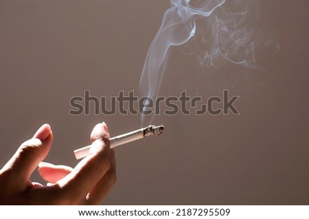 Close-up of a woman's hand holding a cigarette. Tobacco butt with clouds of smoke. Nicotine addiction. The concept of the International Day of smoking cessation.