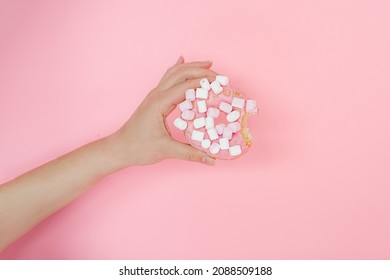 Close-up Of Woman's Hand Holding Donut With Marshmellow On Pink Background. Concept Of Unhealthy Eating. Diet