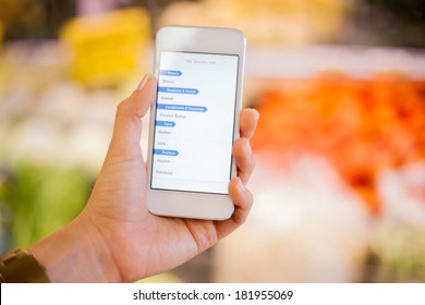 Closeup Of A Woman's Hand Holding A Smart Phone With A Shopping List At A Grocery Store