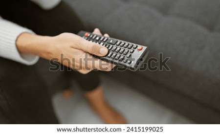 A close-up of a woman's hand holding a television remote control, portraying leisure time at home.
