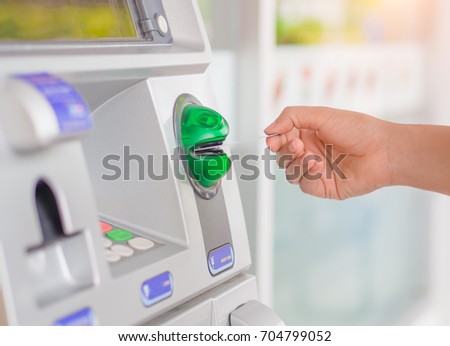 Close-up of woman's hand inserting debit card into an ATM machine.