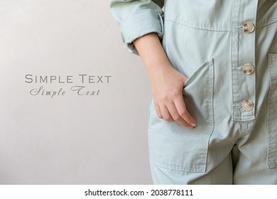 Close-up of a woman's hand in a large pocket of a working cotton light green jumpsuit with large buttons on a beige light background. Eco-style, natural clothing for work and home. Space for text