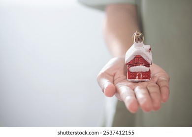 close-up of woman's hand with mini house in her hand. Christmas house concept in red and snow. selling or buying house with discount in December on Christmas Day. - Powered by Shutterstock