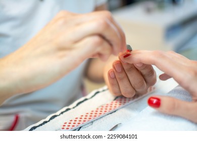 Closeup of a woman's hand in a nail salon receiving a manicure by a beautician with nail file.