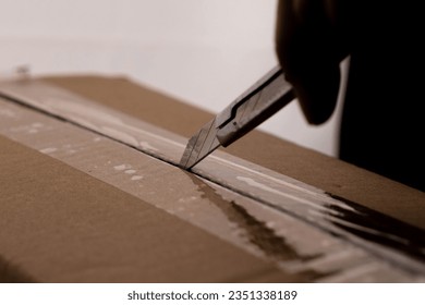 Close-up of woman's hand opening box using cutter. Hands unpacking cardboard boxes in the house.