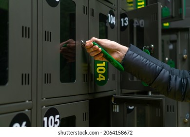 Close-up of a woman's hand opens or closes a numbered storage box in a public place. Cells are dark in color with metal locks and green-yellow keys with numbers. Temporary storage of things