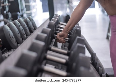 Close-up of woman's hand picking up a dumbbell from a row inside a gym. Sport and fitness concept - Powered by Shutterstock