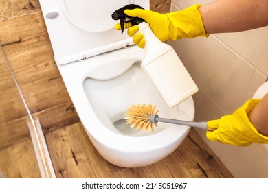 Close-up of woman's hand in protective yellow gloves using a toilet brush and cleaning solution to disinfect a toilet, mock-up of a bottle of cleaner. The concept of cleaning and hygiene in the house
