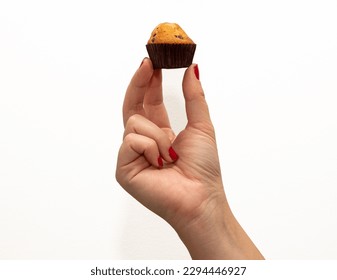 Close-up of a woman's hand with red fingernails holding a mini chocolate chip cupcake on a white background.