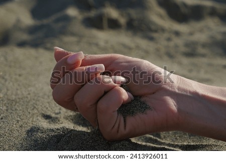 Close-up of a woman's hand releasing falling sand. Sand flows through your hand against the background of sea sand on the beach. The concept of a summer beach holiday