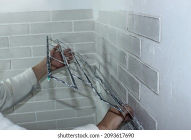 Close-up - a woman's hand removes the stencil from the decorative plaster on the wall. House renovation, decorative brick-like plaster on the wall. Make a brick wall at home with your own hands - Shutterstock ID 2093617690