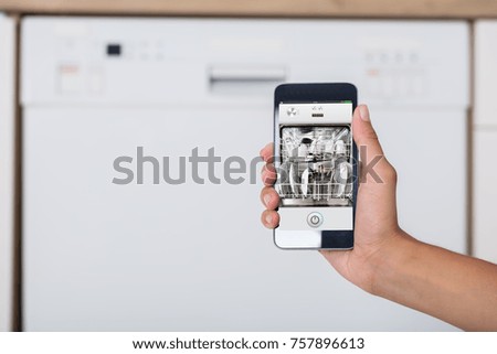 Close-up Of Woman's Hand Showing Dishwasher App On Mobile Phone In Kitchen
