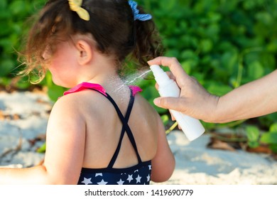Close-up Of Woman's Hand Spraying Lotion On Her Daughter's Back