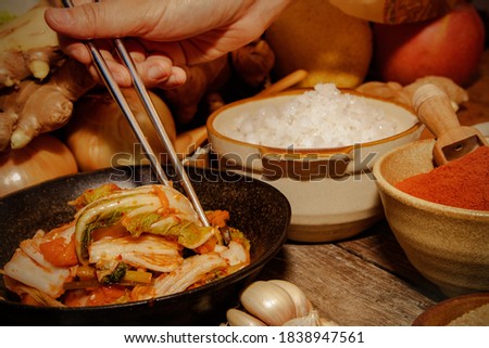 Close-up of a woman's hand using chopsticks to taste kimchi, a traditional recipe of Korean culture.