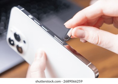 Close-up of a woman's hand using a SIM ejector tool to access the SIM card slot on a sleek white smartphone, crucial for mobile data