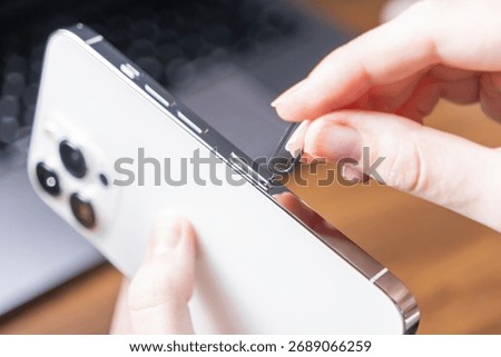 Close-up of a woman's hand using a SIM ejector tool to access the SIM card slot on a sleek white smartphone, crucial for mobile data