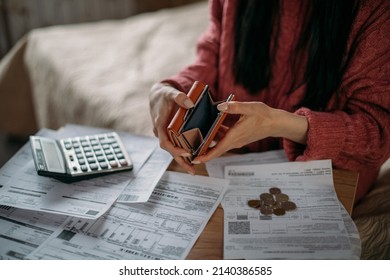 Close-up of woman's hands with empty wallet and utility bills. The concept of rising prices for heating, gas, electricity. Many utility bills, coins and hands in a warm sweater holding an open wallet