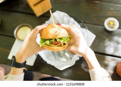 Closeup Of Woman's Hands Holding Burger Over Table At Shop