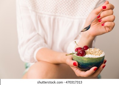 Closeup Of Woman's Hands Holding A Cup With Organic Yogurt With Oats And Cherries. Homemade Vanilla Yogurt In Girl's Hands. Breakfast Or Snack. Healthy Eating And Lifestyle Concept.