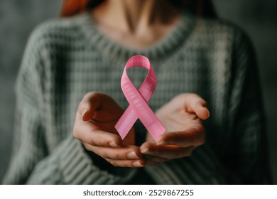 Close-up of a woman's hands holding a pink ribbon, symbolizing cancer awareness and support for women's health. - Powered by Shutterstock