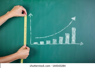 Closeup of woman's hands measuring bar graph with tape on blackboard