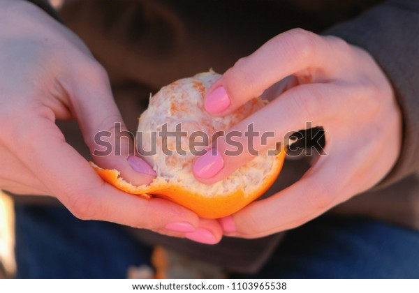 Close-up woman\'s\
hands peels tangerine in\
park.