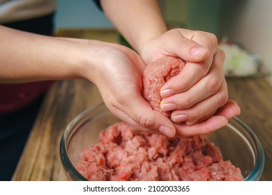 Close-up of a woman's hands preparing ground beef to make hamburgers, the meat is still raw and she is adding the ingredients, nice atmosphere in the kitchen. - Shutterstock ID 2102003365