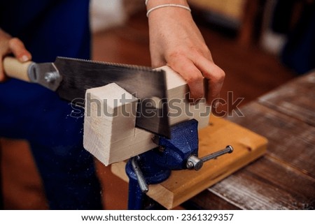 Close-up of a woman's hands sawing a wooden bar. Handmade wood products. Carpenter or joiner at work in a blue apron.