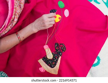 Closeup Of A Woman's Hands Sewing Applique Work Making Doll And Balloon With Chain Stich In Baby’s Quilt Or Bed Sheet. Concept Of Self Employment Woman And Female Entrepreneurs In India.