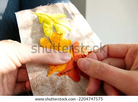 Close-up of a woman's hands sewing  applique work with a design of autumn leaves.