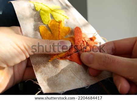 Close-up of a woman's hands sewing to produce applique work of autumn leaves.