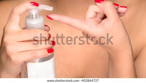 Closeup womans hands squeezing cream\
from bottle onto tip of finger, bare skin\
background.