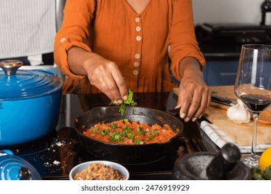 Close-up of a woman's hands standing by the stove, adding chopped basil to fresh tomato sauce - Powered by Shutterstock