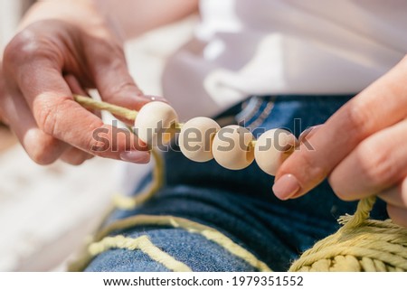 Close-up of a woman's hands stringing wooden beads on cotton thread for macrame.Handmade concept.Selective focus with shallow depth of field.